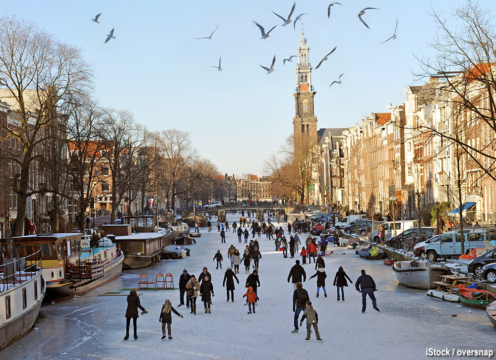 Amsterdam, Netherlands - February, 10th 2012: The Prinsengracht canal frozen over (a rare occurrence) with locals and visitors skating and walking on the ice. The landmark Westerkerk church in the distance